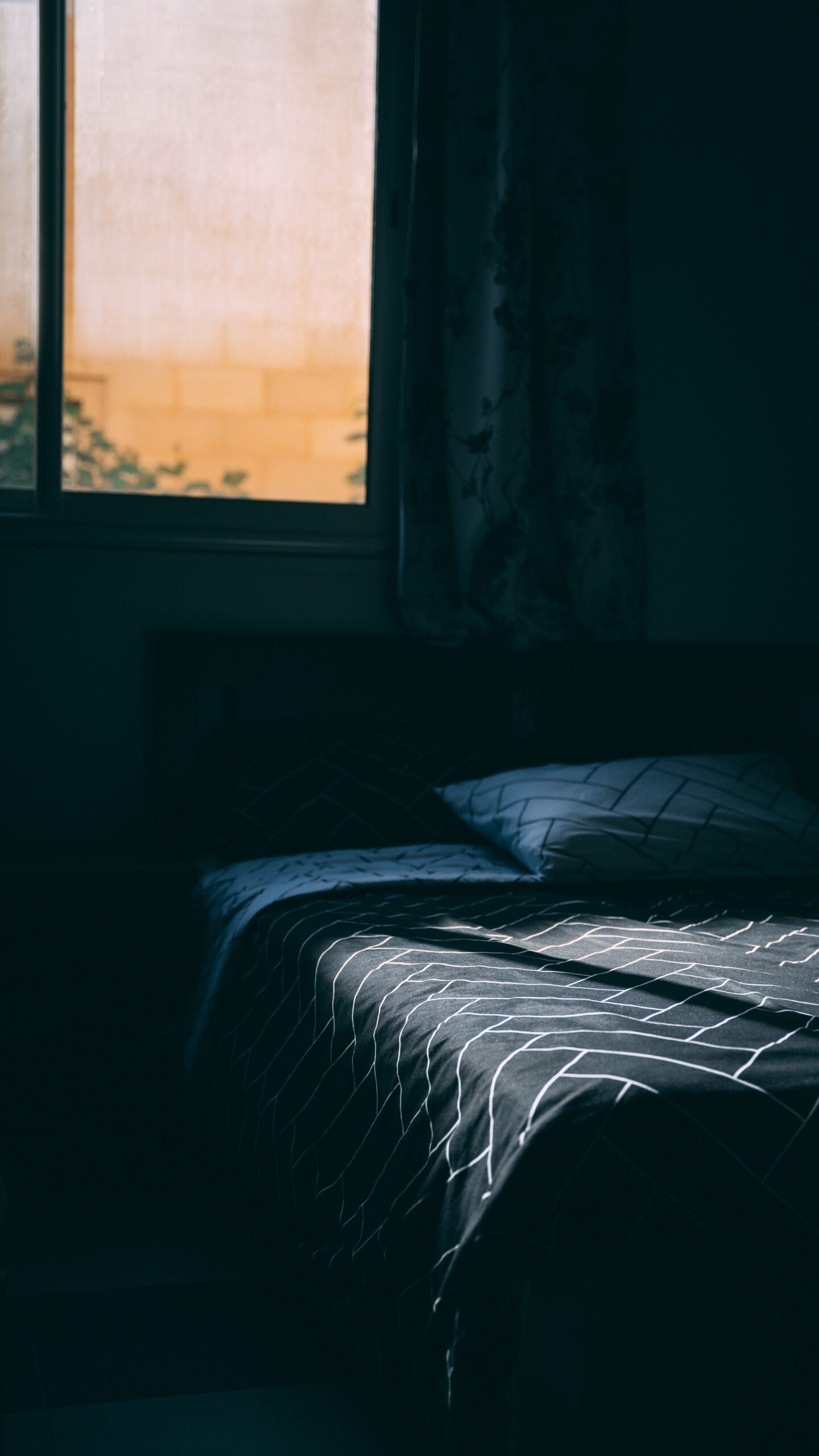 Chambre plongée dans l'obscurité en pleine journée, lumière extérieure filtrée par la fenêtre, symbole du sommeil décalé à l'adolescence