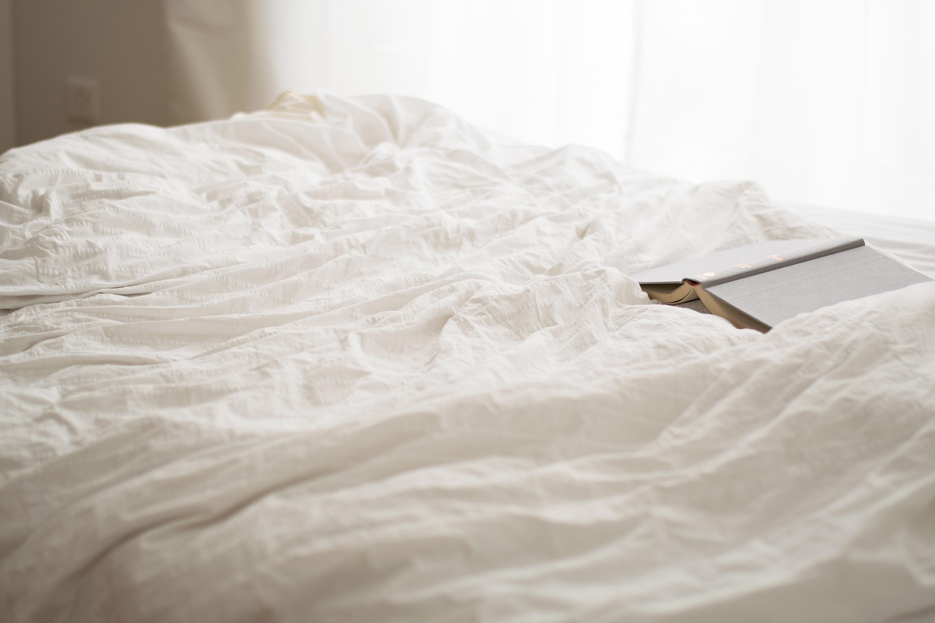 Lit défait avec un livre posé, lumière douce du matin, symbole d'un nouveau départ possible après une rentrée difficile